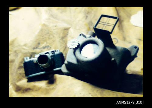 Colour photograph of a Leica camera and an underwater camera sitting on a yellow sheet of plastic