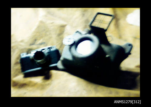 Colour photograph of a Leica camera and an underwater camera sitting on a yellow sheet of plastic