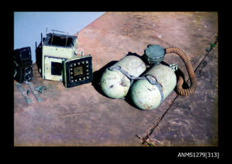 Colour photograph of a Rolleiflex camera, green underwater camera case and two green air tanks, sitting in a row on the cement