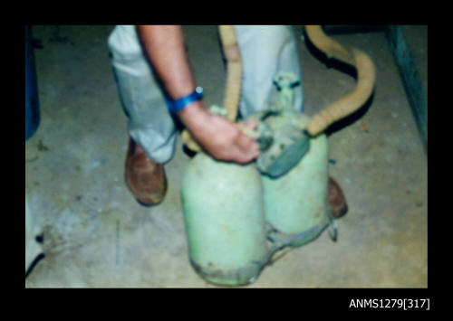 Colour photograph of two green diving air tanks, being held upright by a man