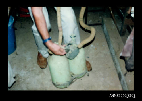 Colour photograph of two green diving air tanks, being held upright by a man