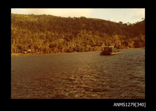 Colour photograph of a green boat, in the water close to the shoreline, on Pearl Island