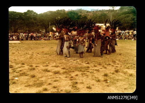 Colour photograph of a ring of Papua New Guinean people wearing traditional dress at the Pacific Festival, with hundreds of onlookers, on Pearl Island