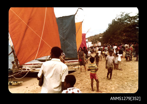 Colour photograph of boats with coloured flags lined up on the beach for the Pacific Festival on Pearl Island, with onlookers standing on the sand