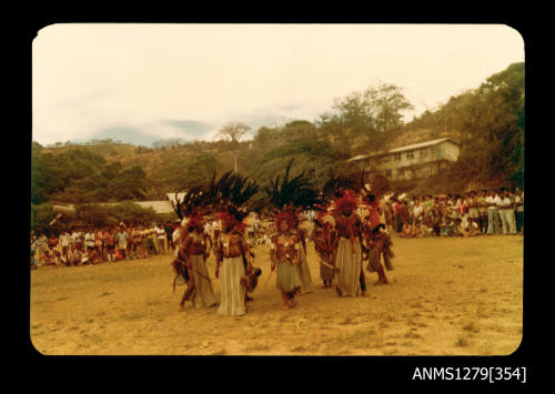 Colour photograph of several Papua New Guinean people in traditional dress, standing in a ring, surrounded by hundreds of onlookers, taken at the Pacific Festival on Pearl Island