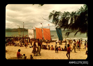 Colour photograph of many Papua New Guinean people standing and sitting on the beach during the Pacific Festival on Pearl Island, with boats with coloured sails on the beach
