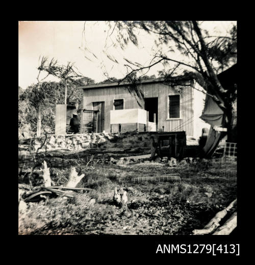 A small house or shed, with equipment sitting out the front, including several rolled sheets of wire