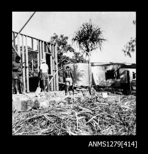 Three men building a shed or house, with a large water tank in the background