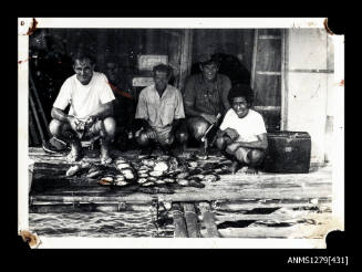 Photograph of five men sitting on a wharf with a pile of pearl shells