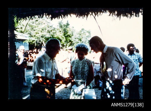 Queen Elizabeth II, Prince Philip and Denis George, with George demonstrating something in his hands, during their visit to Papua New Guinea in 1977