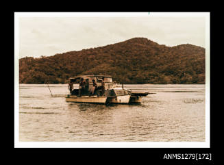 Colour photograph of a grey and cream coloured boat in the water, with four Papua New Guinean men on board