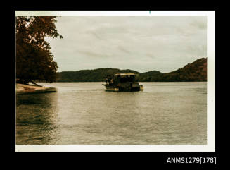 Colour photograph of a boat in the water near the shoreline, with several people on the boat