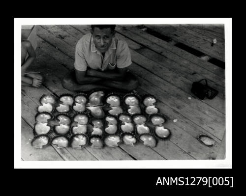 A man sitting on a wood floor in front of lined up pearl shells