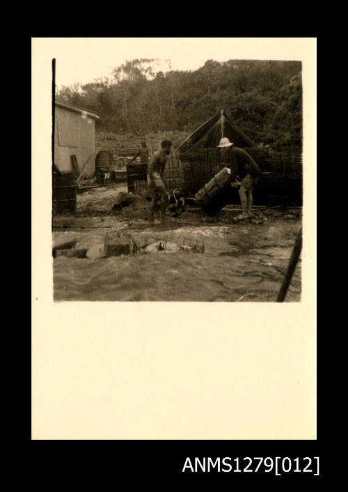 Three men, with one moving a metal drum, surrounded by equipment