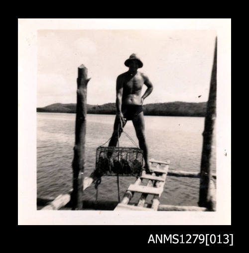 Photograph of  Denis Geroge standing on a pearl raft, holding up a pearl cage