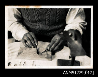 A man using pearl seeding tools on a wooden board, with a pearl shell clamp in the foreground