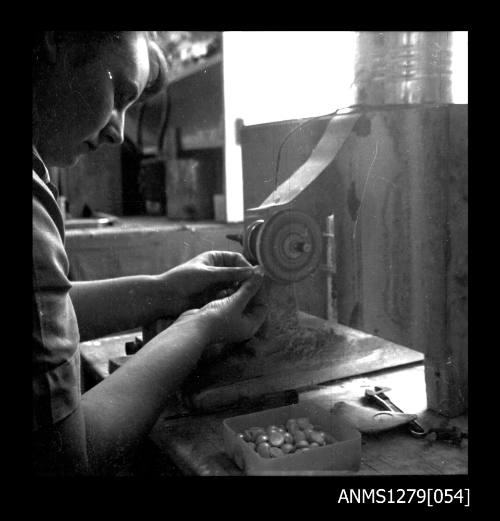 A person using a grinder, with a container of half pearls (or mabe pearls) on the table next to the grinder