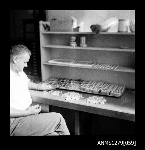 A man, possibly Denis George, sitting at a desk with containers, half pearls (or mabe pearls) and nuclei