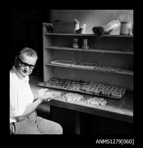 A man, possibly Denis george, sitting at a desk with containers, half pearls (or mabe pearls) and nuclei