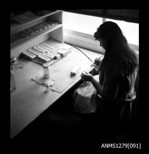 A woman sitting at a desk using an air brush to spray the insides of half pearls (or mabe pearls)