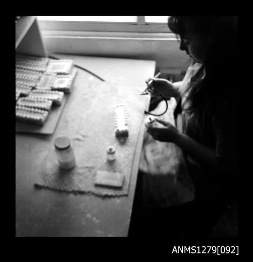 A woman sitting at a desk using an air brush to spray the insides of half pearls (or mabe pearls)