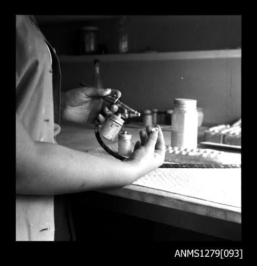 A close up of a woman hands whilst spraying the insides of half pearls (or mabe pearls) with an air brush