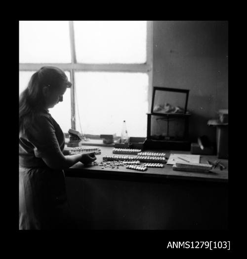 A woman standing next to a desk, possibly removing half pearls (or mabe pearls) from half pearl holders