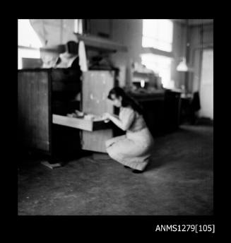 A woman crouching down at an opened draw in a cabinet