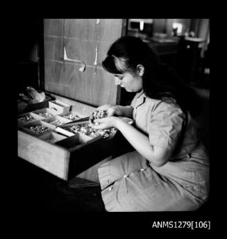 A woman crouching down to a drawer filled with trays of half pearls (or mabe pearls)