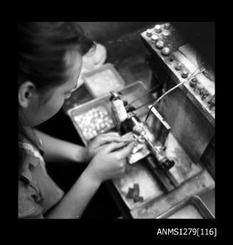 A woman using a grinding machine, with a container of half pearls (or mabe pearls) beside the machine