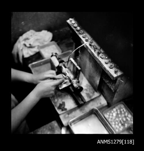 A woman using a grinding machine, with half pearls (or mabe pearls) visible in a container to the side