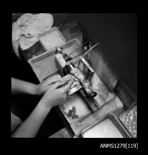 A woman using a grinding machine, with half pearls (or mabe pearls) visible in a container to the side