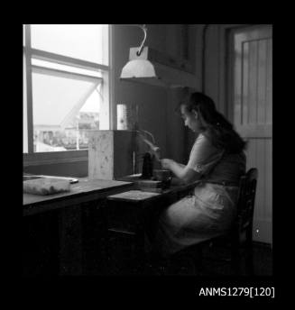 A woman sitting at a desk using a grinding machine, with a water can above the machine