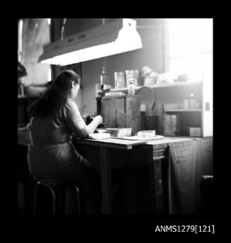 A woman working at a work bench metal containers and various pieces of equipment