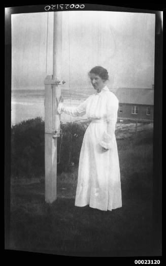 Unidentified woman, possibly related to Captain Edward R Sterling, standing next to a flag pole