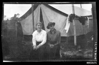 Two women seated in front of a tent