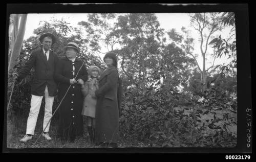 Man, two women and a girl in front of trees and shrubs