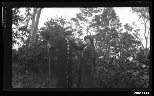 Two women standing in front of trees and bushes