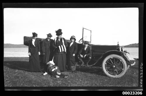 Three women, two men and one girl in front of a car