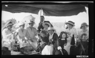 Women, man and children seated under a tarpaulin