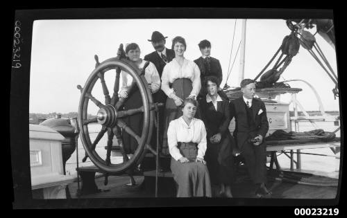 Seven men and women standing around a ship's wheel