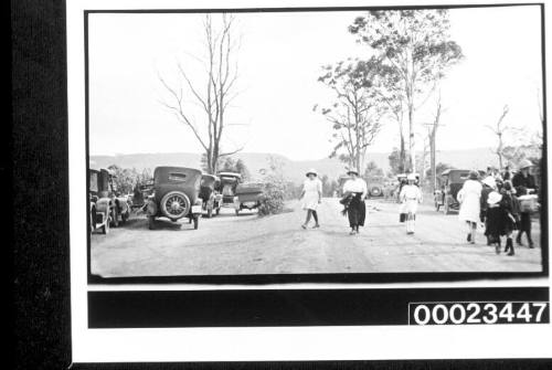 A group of women and children on a dirt road lined with motor vehicles