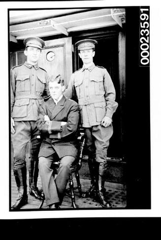 Ships and steamer crews, two men in military uniform on either side of seated man in naval uniform