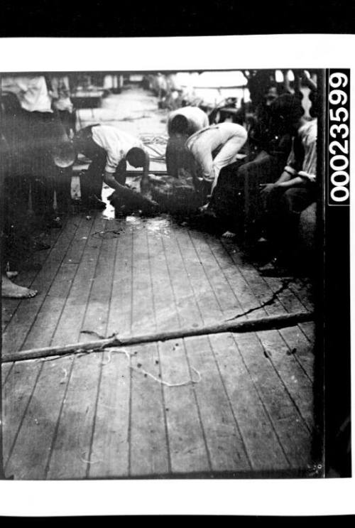 Ships and steamer crews, three men leaning over object on deck