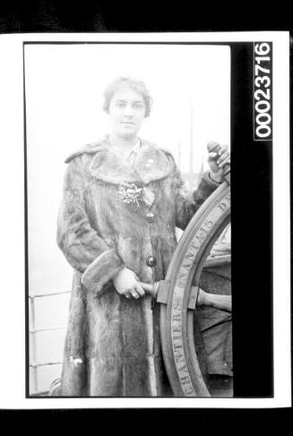 Woman in fur coat standing next to whip's wheel