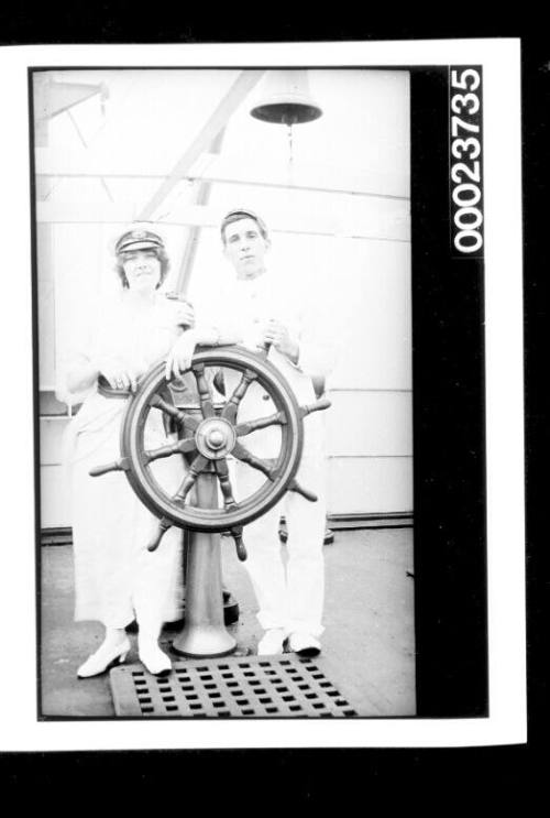 Man and woman standing with a ship's wheel