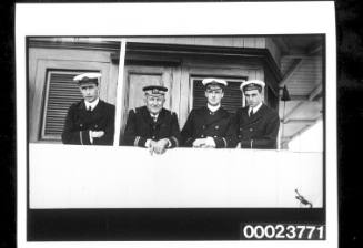 Four officers in a row leaning over white wooden rail