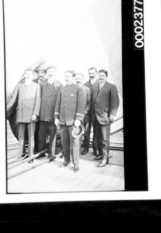 Scene on wooden deck of ship with large flag and group of men