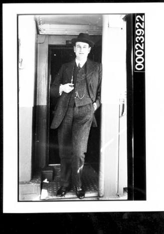 Man standing in doorway wearing suit and holding a pipe