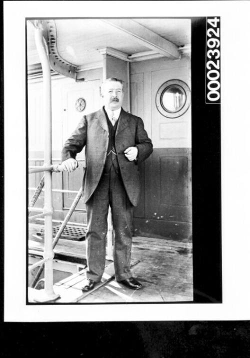 Man standing on deck wearing a a suit and boater and holding papers